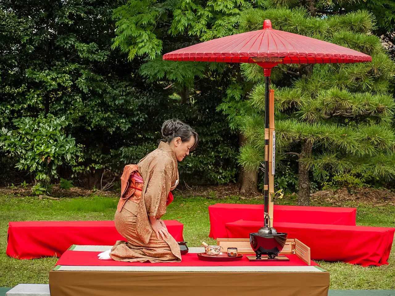 A Japanese tea ceremony performed outdoors under a red parasol