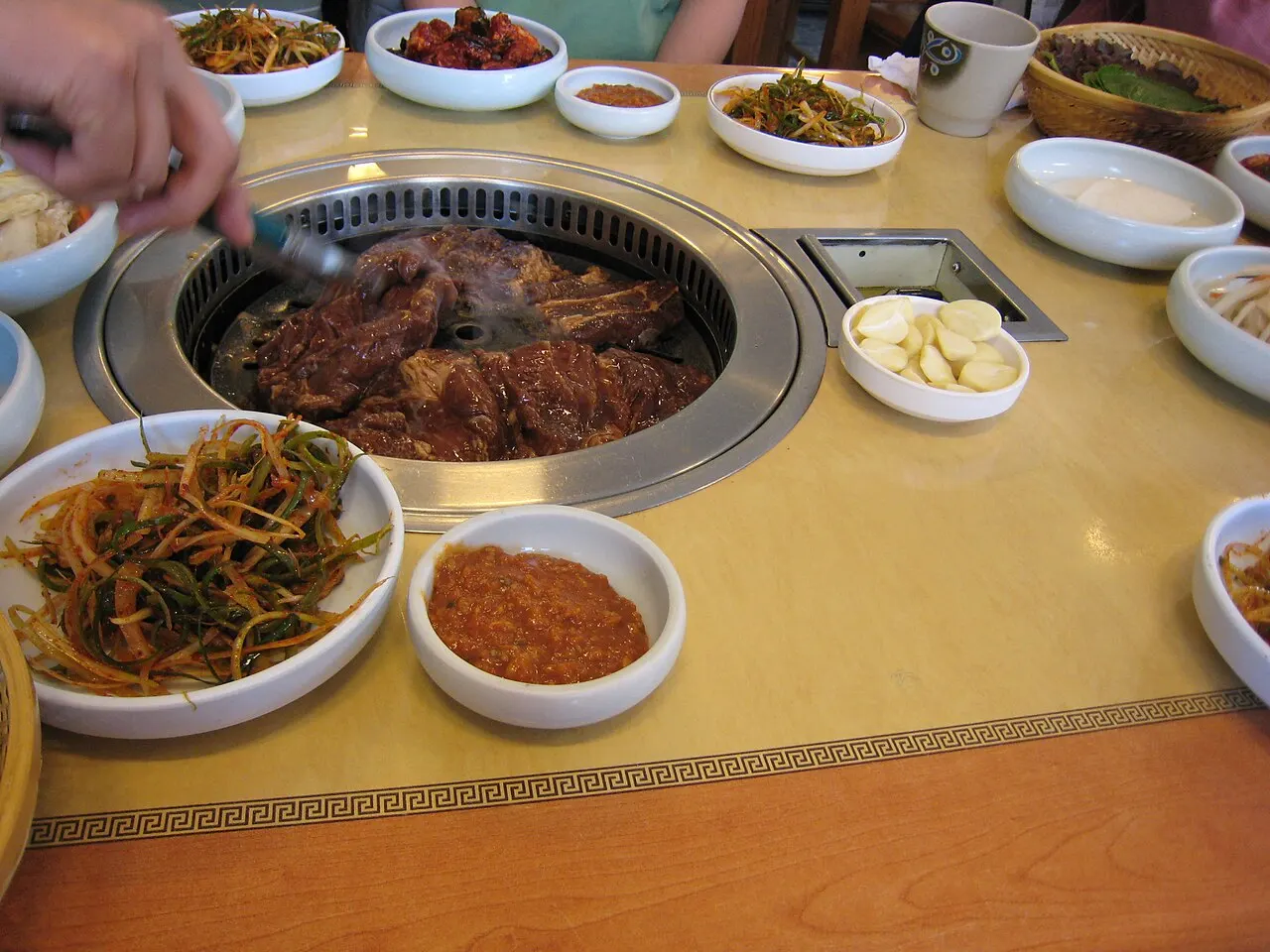 Galbi grilling at a Korean barbecue table with banchan side dishes