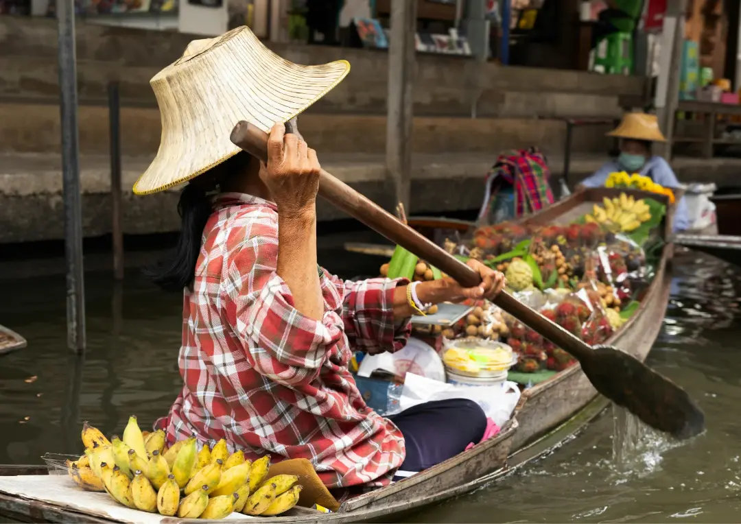A vendor paddling a fruit boat at a floating market near Bangkok